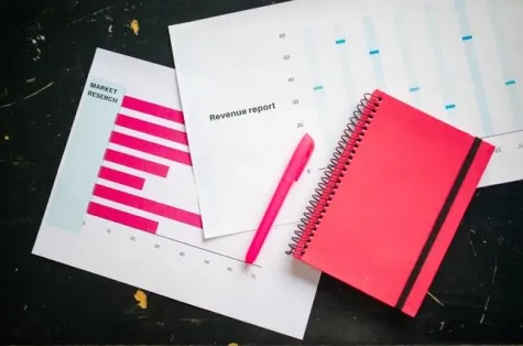 Overhead shot of a desk with charts, a red notebook, and a pen for business analysis.